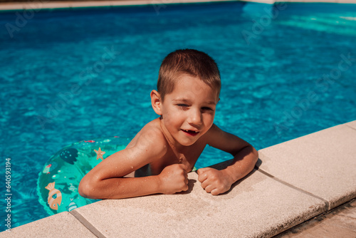 A little boy climbs out of the pool. A child bathes at noon in the heat