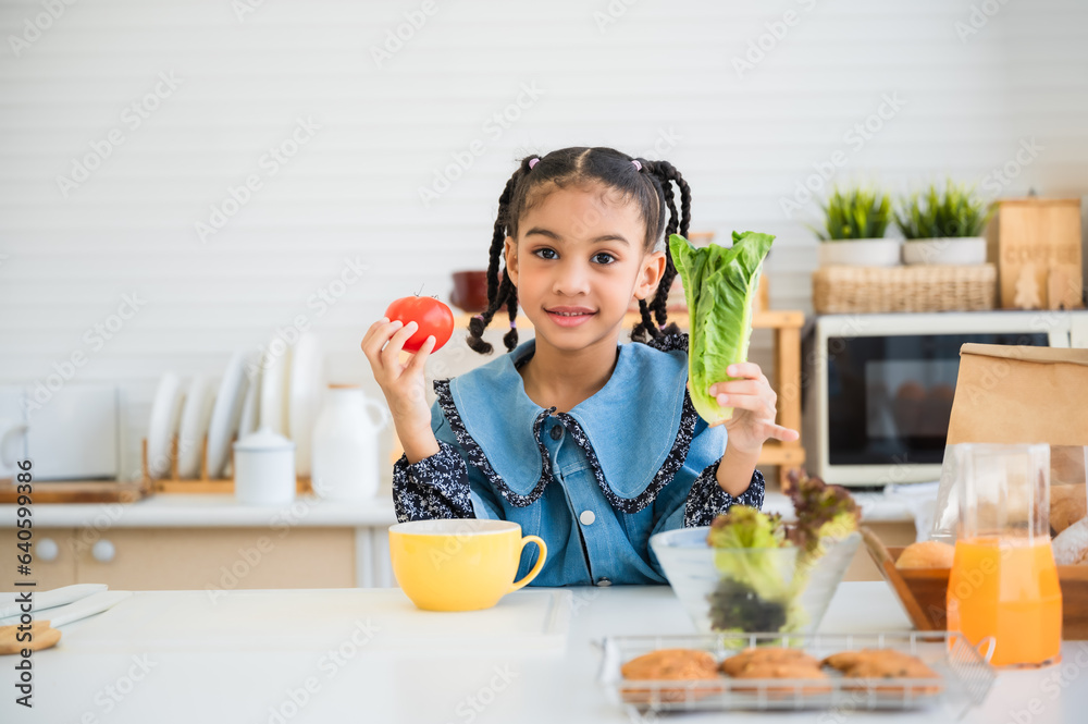 Happy pretty small child girl holding lettuce and red tomato in the kitchen room at home. Happy pretty small child girl holding lettuce and red tomato in the kitchen room at home.