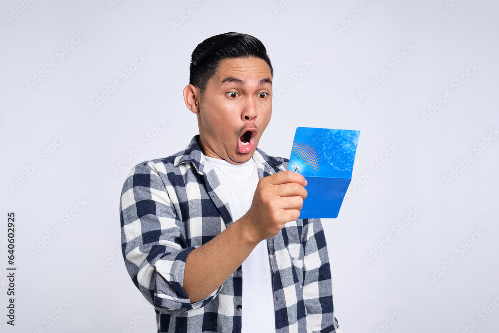 Surprised young Asian man in casual shirt looking at saving account passbook isolated on white background Surprised young Asian man in casual shirt looking at saving account passbook isolated on white background