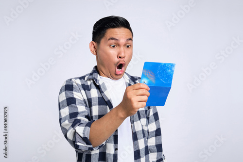 Surprised young Asian man in casual shirt looking at saving account passbook isolated on white background