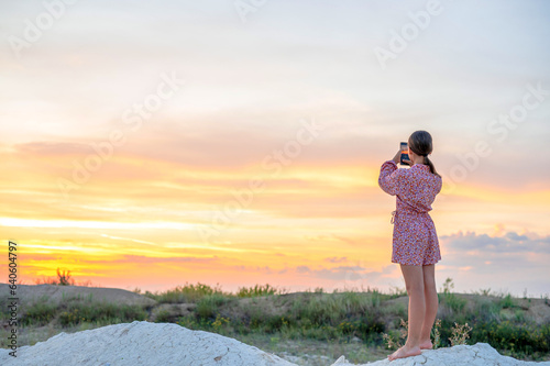 teenage girl photographs the sunset on a mobile phone, recreation and entertainment for children in nature.