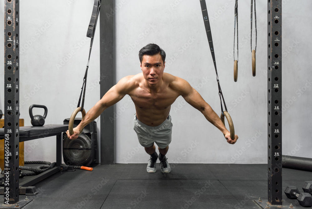 Fototapeta premium Athlete exercising on gymnastic rings in a well-equipped, modern gym. The man displays strength and determination, his muscles ripple with exertion.
