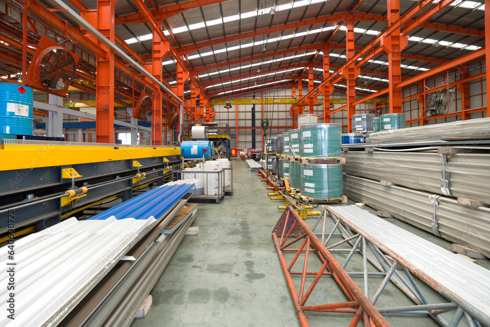 A gargantuan warehouse brims with a labyrinth of gleaming steel beams crisscrossing overhead, creating a metallic canopy. There are steel sheet roll and metal sheets on the floor. A gargantuan warehouse brims with a labyrinth of gleaming steel beams crisscrossing overhead, creating a metallic canopy. There are steel sheet roll and metal sheets on the floor.