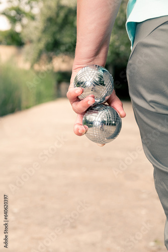 woman two pétanque balls held in her left hand in vertical photo.