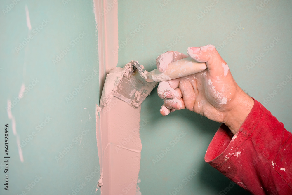 Hand with a spatula. Worker trowels putty on drywall. Puttying plasterboard walls with a spatula indoors
