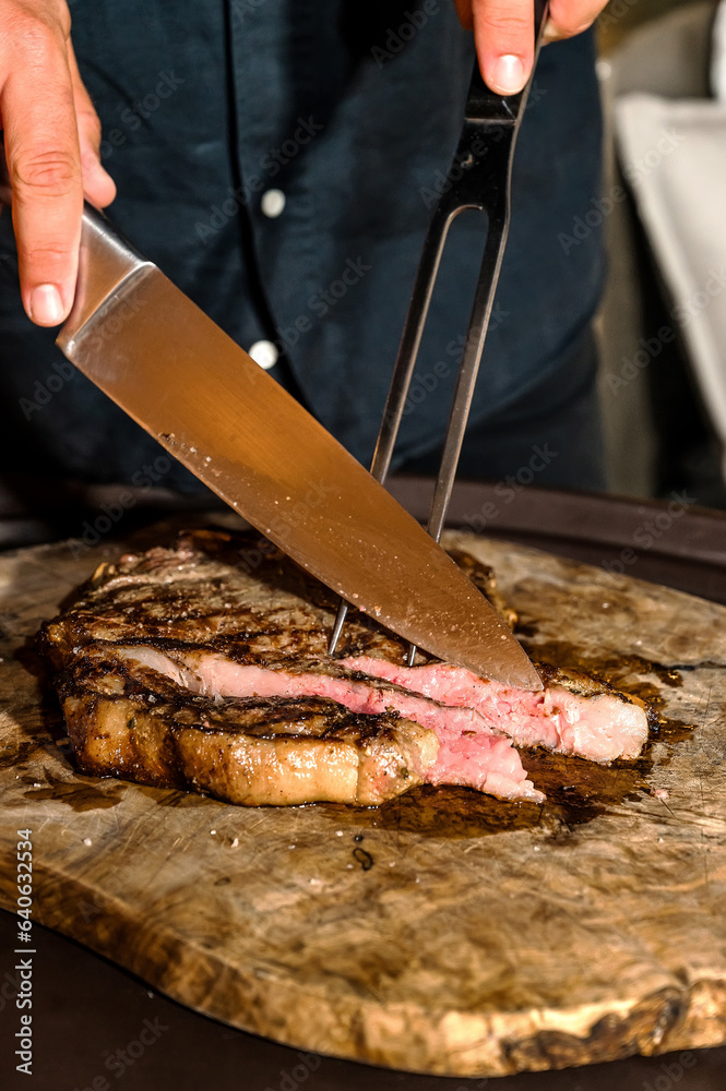 Hand using large knife, slicing raw meat on wooden board. Restaurant cooking concept. Close up photo. Selective focus.