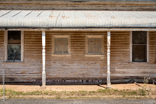 An old faded and flaking painted  weatherboard house in a rural town in Victoria Australia with symmetrical windows and columns holding up a patio corrigated roof