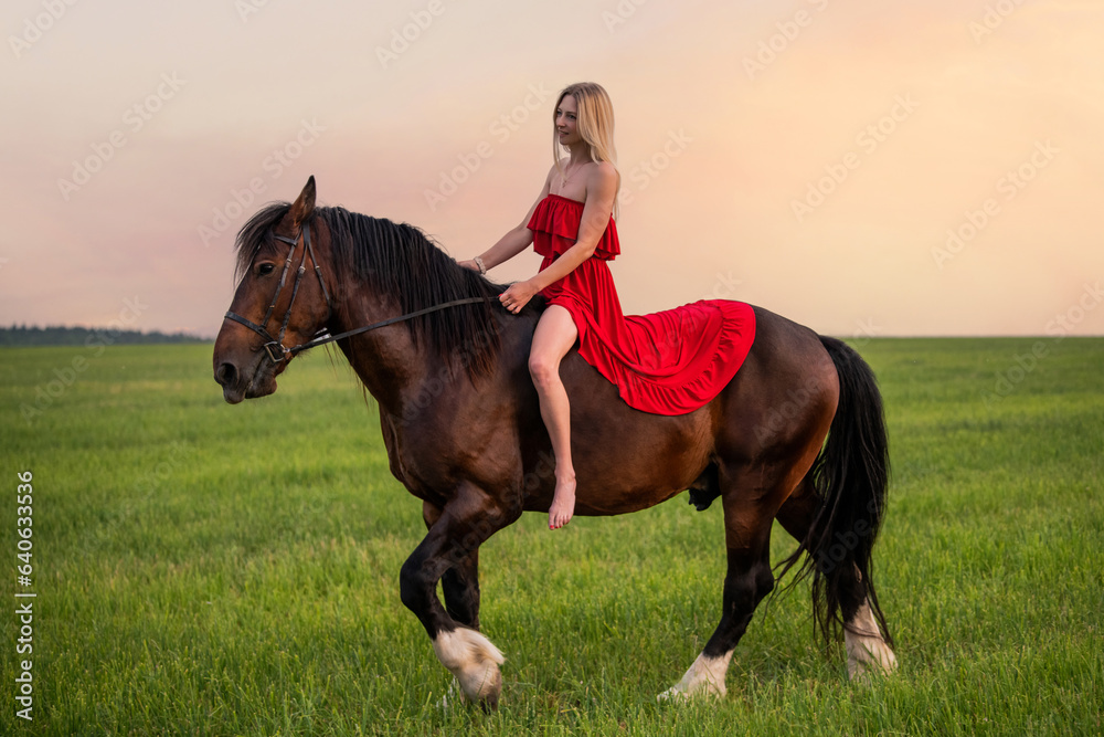 A young woman in a red dress walks with a horse in a field at sunset A young woman in a red dress walks with a horse in a field at sunset
