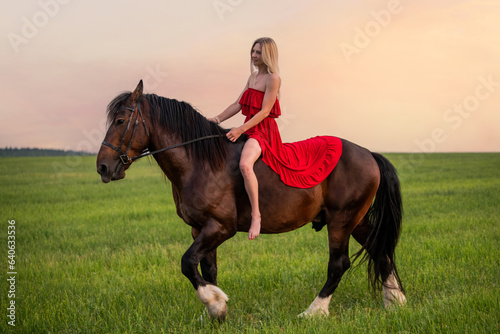 A young woman in a red dress walks with a horse in a field at sunset