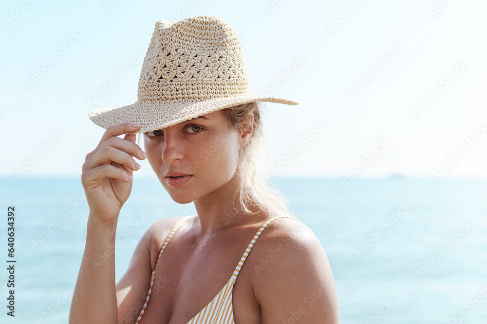 Woman radiates summer vibes wearing yellow striped bikini and a straw hat, enjoying her time on the sandy beach