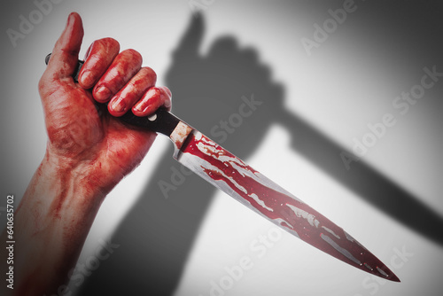 Male hand with a knife in blood stains casting shadow on white background