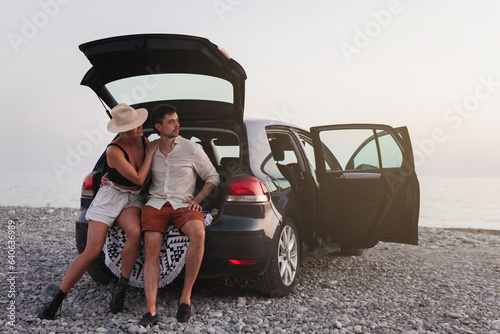 Couple of travelers standing beside their car on a pebble beach during their road trip © blackday