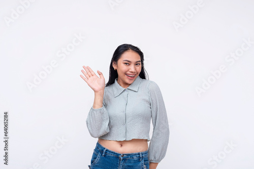 An expressive young asian woman waving her hand saying hello. A chummy greeting from a friend. Isolated on a white background. photo