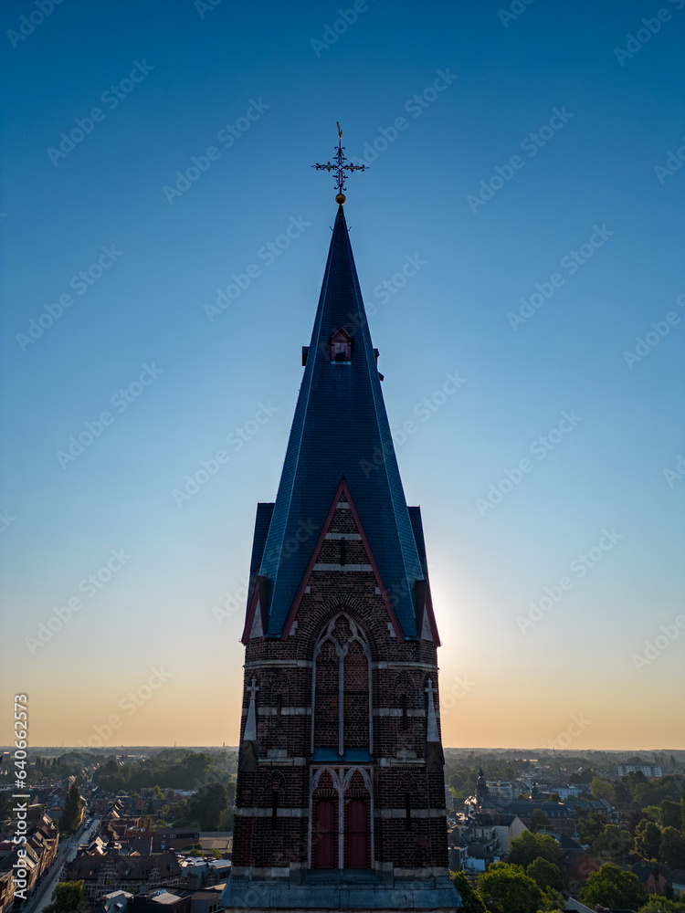 Capture the ethereal beauty of a serene morning with this breathtaking aerial photo. The silhouette of a church tower stands tall against the backdrop of a radiant sunrise, symbolizing hope, serenity