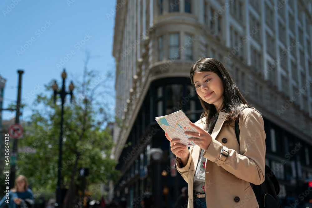 low angle view of smiling asian Chinese woman tourist reading guide map with triangular Phelan office building at background in san Francisco California usa on a sunny day