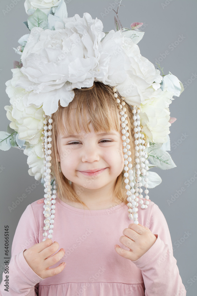 Pretty kid girl in white flower hat smiling on grey background Pretty kid girl in white flower hat smiling on grey background
