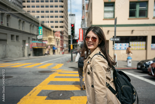 smiling asian korean business lady wearing sunglasses turning to look at camera while waiting to cross the street near chinatown in san Francisco California usa on windy day © PR Image Factory