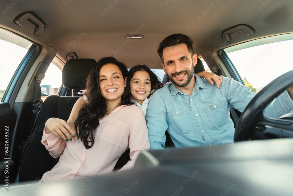Happy european family with child girl sitting inside car and smiling at camera, enjoying road trip in new automobile