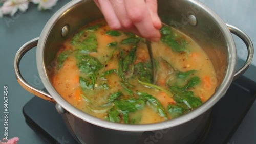 Female hands knead green soup with spinach on coconut milk with a spoon. Close-up of the table. Cooking in the kitchen