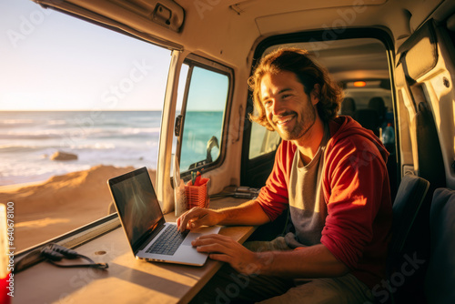 Handsome young digital nomad using a laptop computer in camper van on sunny day. Man working remotely with his laptop. Digital nomadic life. photo