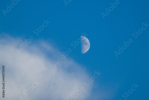 Beautiful half moon on the blue sky with a white cloud at a summer day
