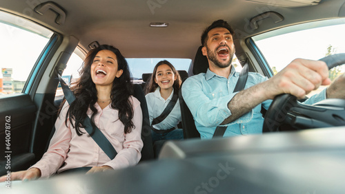 Excited european family of three riding car and singing, parents and daughter enjoying auto ride together on weekend