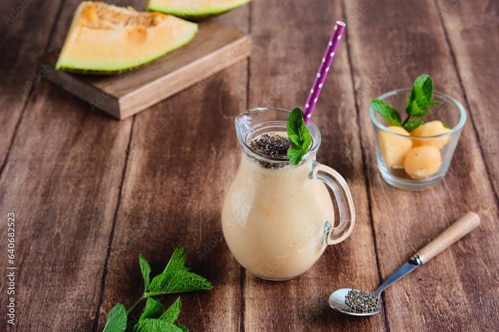 Melon smoothie with chia seeds in a serving jug on a brown wooden background. Melon recipes. Refreshing soft drinks. Melon smoothie with chia seeds in a serving jug on a brown wooden background. Melon recipes. Refreshing soft drinks.