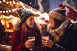 Two female friends having wonderful time on traditional Christmas market on winter evening. Beautiful girls drinking hot beverages in Christmas town decorated with lights.