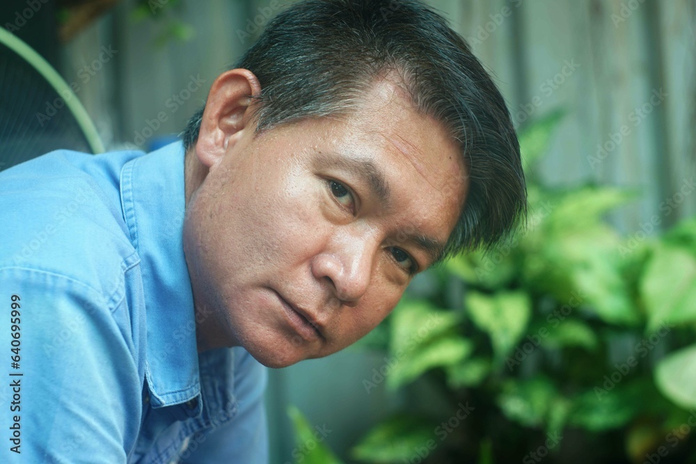 Obraz premium Close up beside veiw of a portrait of a middle-aged Asian man in a blue shirt, man alone concept.