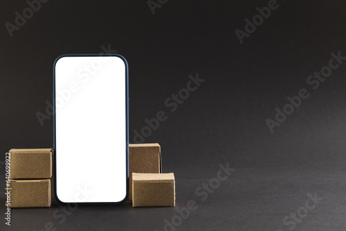 Smartphone with blank screen and cardboard boxes with copy space on black background
