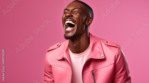 Young man laughs against a pink background.