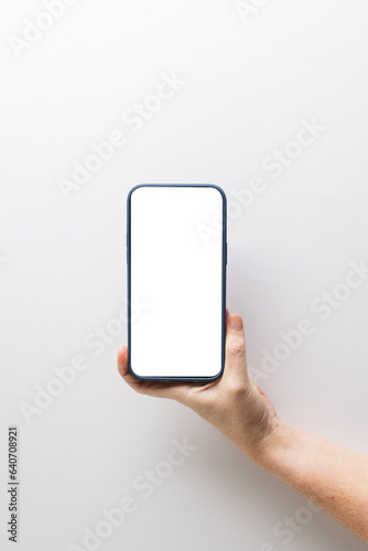 Vertical image of caucasian woman holding smartphone with blank screen on white background