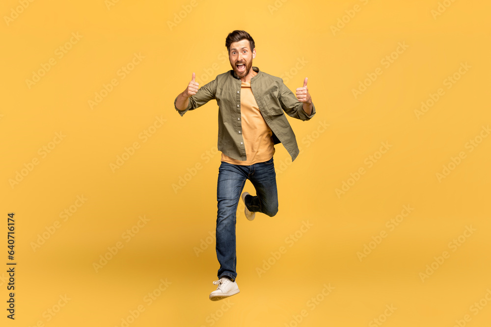 Excited european middle aged man running towards camera, smiling and showing thumb up over yellow background
