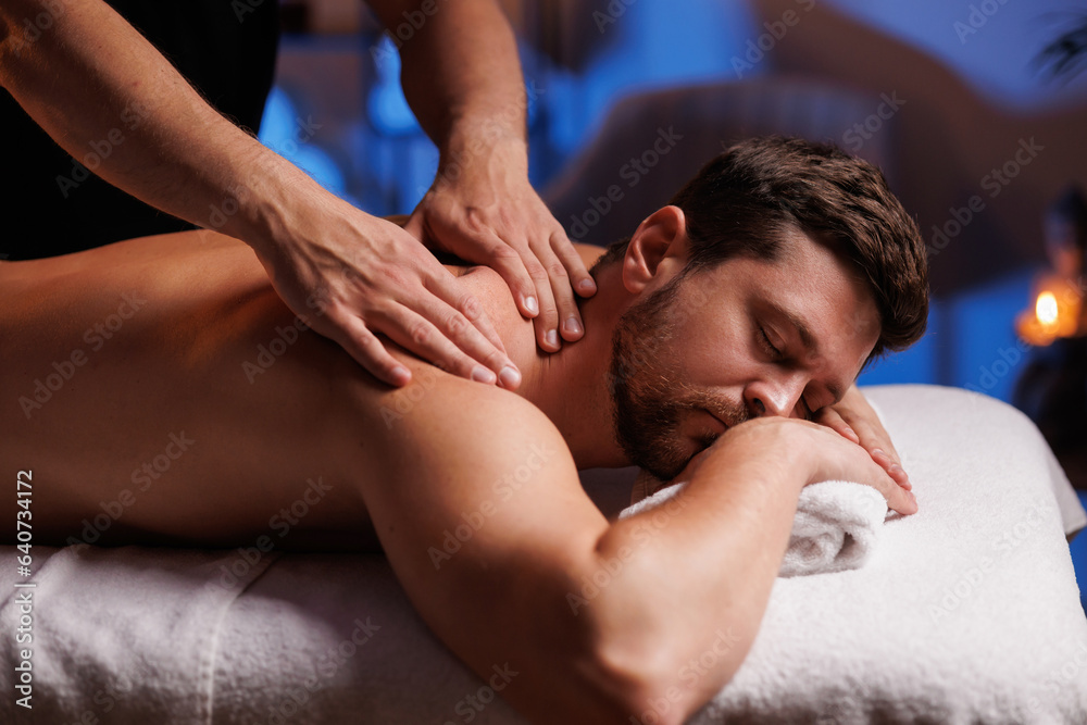 Handsome man having restorative back massage in spa salon, enjoying relaxing atmosphere, recharging after work. Masseuse gives therapeutic back massage to a visitor, the concept of healthy lifestyle. Handsome man having restorative back massage in spa salon, enjoying relaxing atmosphere, recharging after work. Masseuse gives therapeutic back massage to a visitor, the concept of healthy lifestyle.