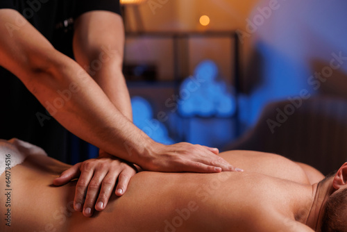 Extreme closeup of masseurs male hands gently pressing hands along clients back. Concept of aesthetic relaxing massage in spa salon  recovery  reboot.