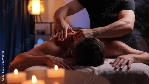 Physiotherapist massaging male patient with damaged shoulder muscle, treating sports injuries. Relaxing professional shoulder massage in cozy atmosphere, reboot on the weekend, end of difficult week.