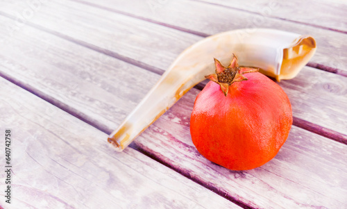 A shofar with a pomegranate rimmon on a white wooden surface. A symbol of the Rosh Hashanah holiday. Suitable for shana tova greeting card and Yom Kippur. with free space for text