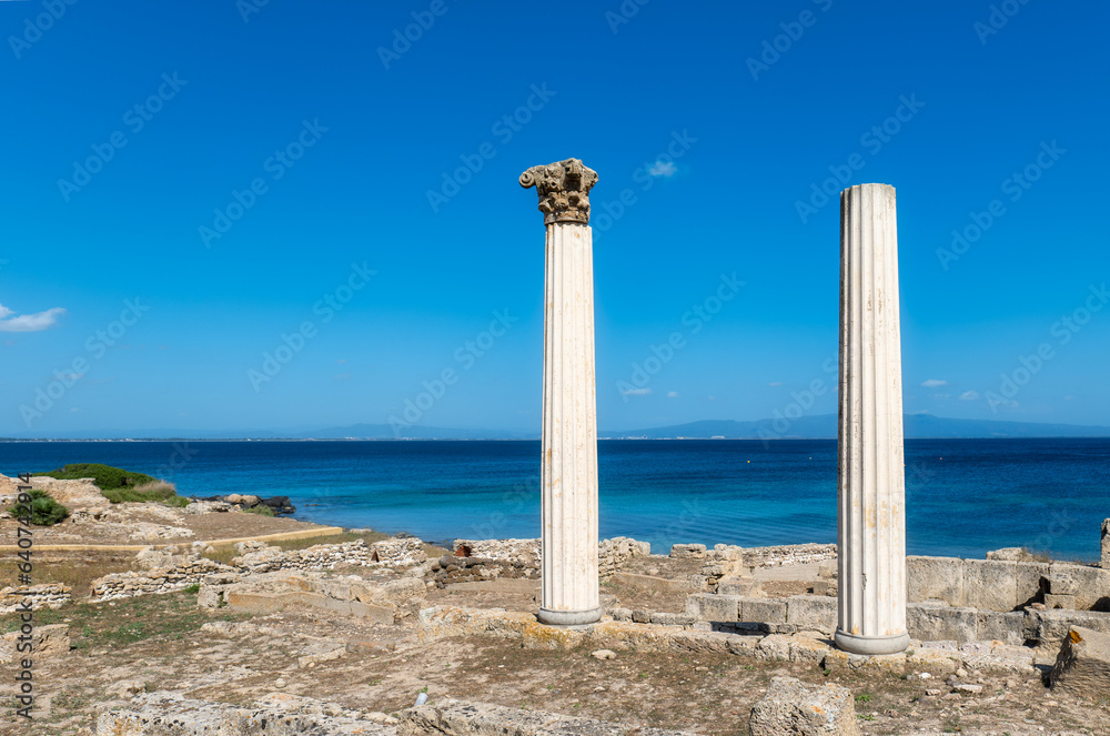A panoramic view of ancient Roman columns overlooking azure Mediterranean waters on Sardinia's Sinis Peninsula.