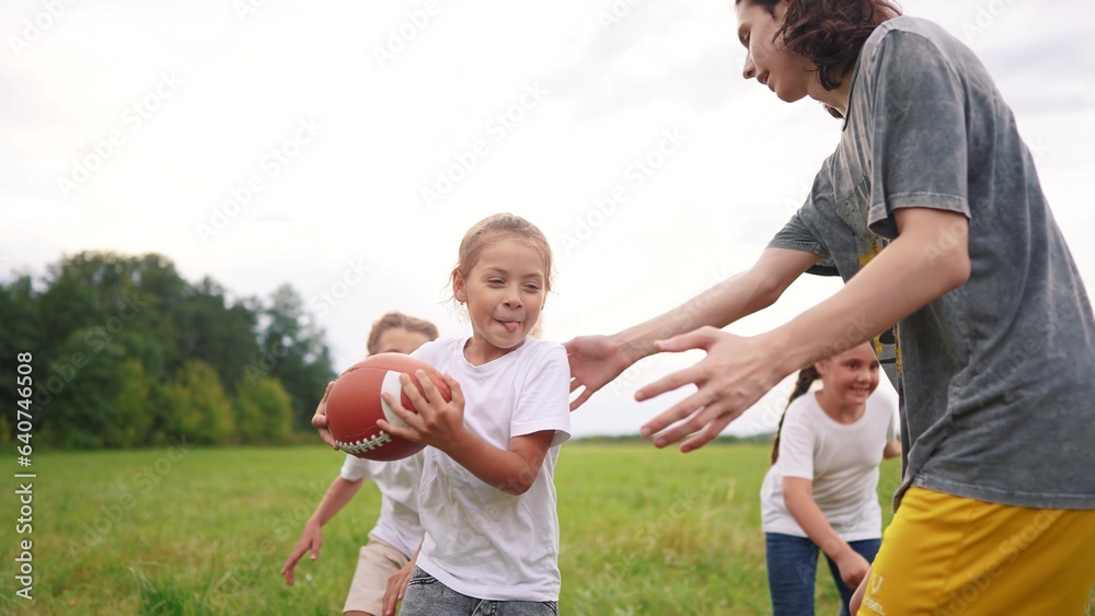 a group of children run on the grass in the park with a ball. happy family childhood dream concept. children run on the green grass and play american lifestyle football together. kids have fun a group of children run on the grass in the park with a ball. happy family childhood dream concept. children run on the green grass and play american lifestyle football together. kids have fun
