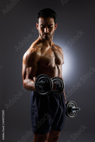 Muscle, strong and studio man with dumbbell challenge results, arm workout development and body fitness progress. Dark shadow, gym equipment and sports athlete with training focus on grey background © Joanrae P/peopleimages.com