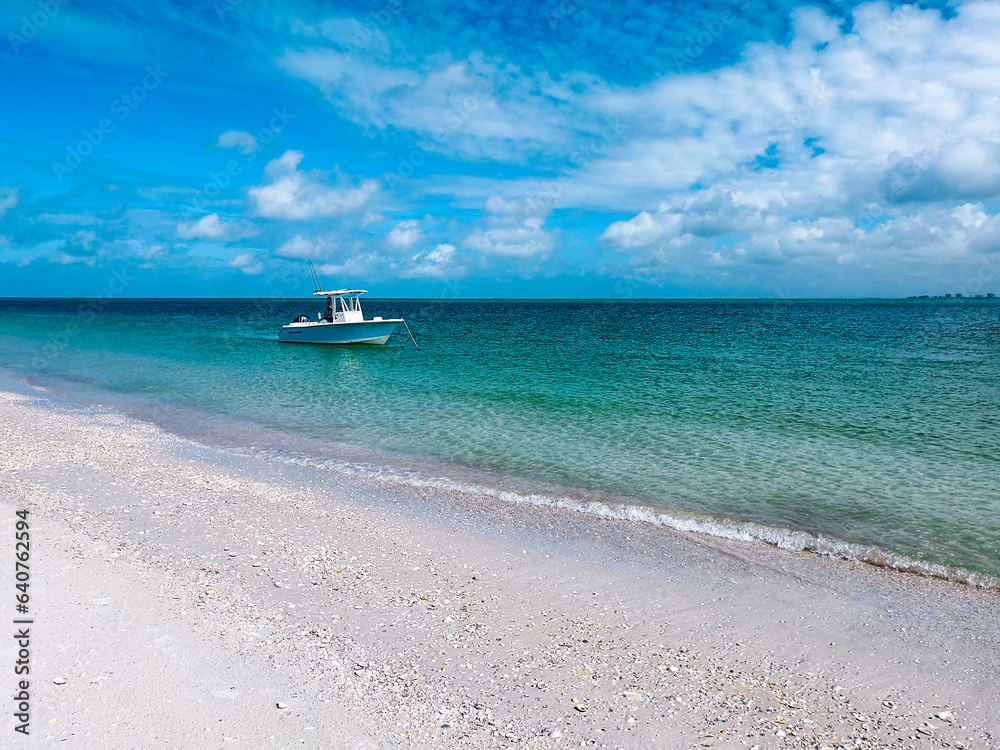 A small blue boat is motoring through calm ocean waters on a moderately cloudy day at the beach.