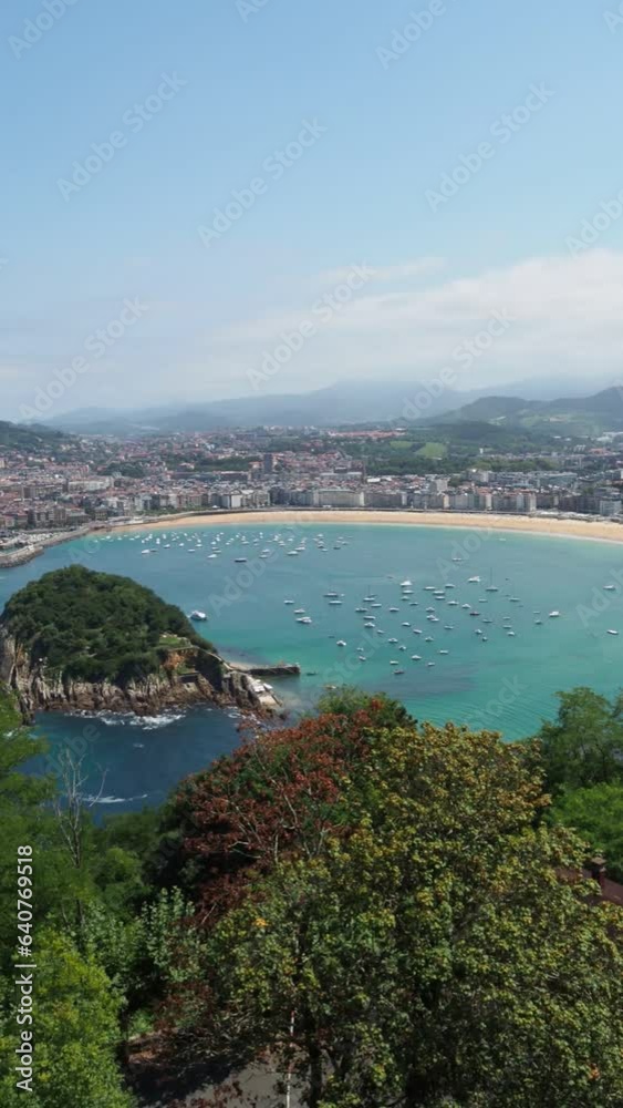 Aerial view of La Concha bay in San Sebastian city during summer with boats on the shore and the beach. Vertical panoramic video with copy space of beach city with turquoise water. Aerial view of La Concha bay in San Sebastian city during summer with boats on the shore and the beach. Vertical panoramic video with copy space of beach city with turquoise water.