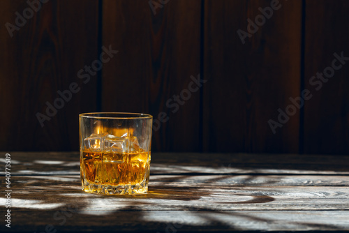 A glass of whiskey and ice stands on an old wooden table