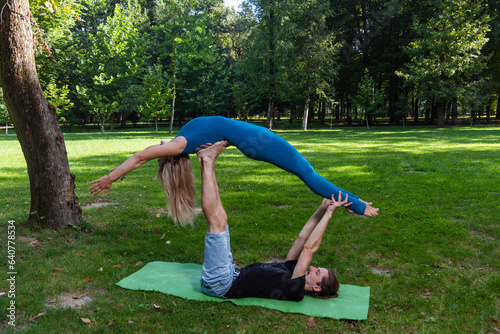 Boy and girl doing acro yoga outdoors in summer in public park