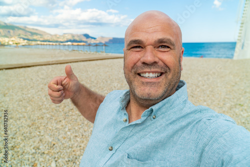 Happy man takes a selfie, with a beach on background.
