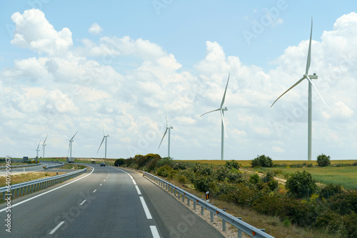 Wind turbines stand along the road against the background of clouds.
