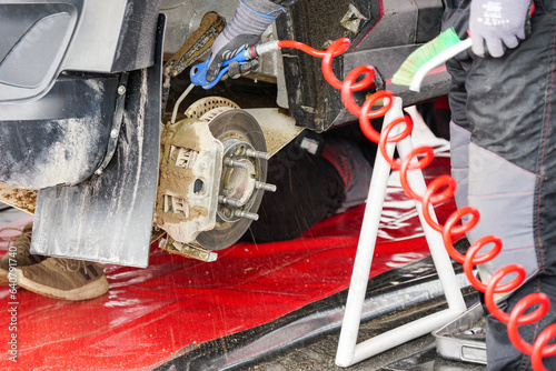 Bild auf Leinwand Rally car maintenance in service park, blowing off mud from the brake caliper wi