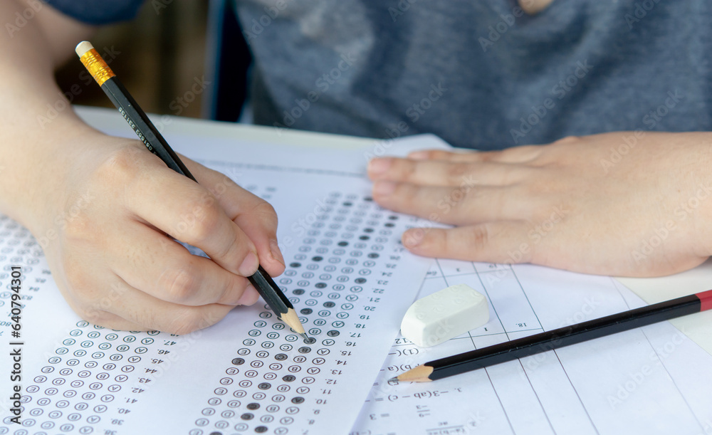 Fototapeta premium Students hand holding pencil writing selected choice on answer sheets and Mathematics question sheets. students testing doing examination. school exam