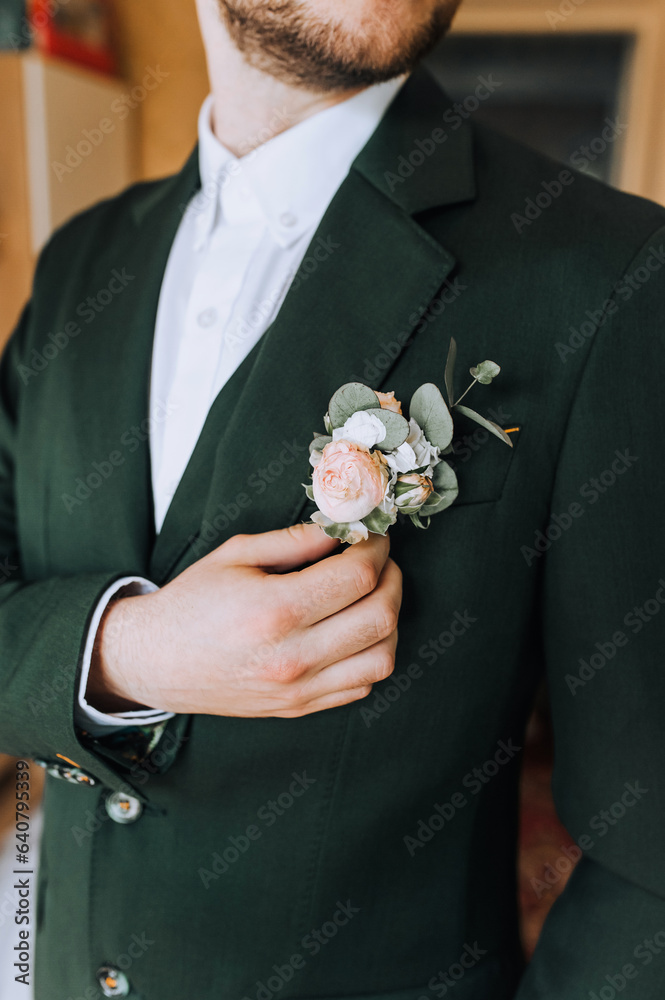 Portrait of a stylish, fashionable groom, a man in a green suit, a white shirt with a boutonniere on his jacket. Close-up wedding photography.