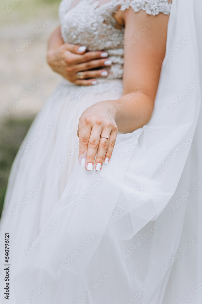 The bride holds a white lace dress in her hand with a golden ring on her finger. Wedding photography, portrait. The bride holds a white lace dress in her hand with a golden ring on her finger. Wedding photography, portrait.
